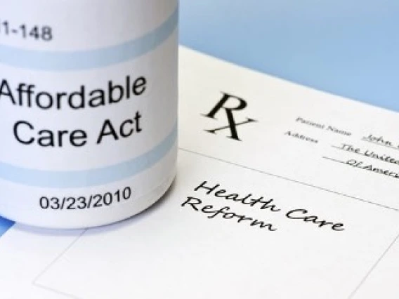 prescription bottle with the words affordable care act sits on top of a doctors prescription