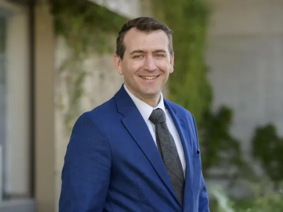 portrait of Benjamin Brady wearing a blue suit in front of some greenery