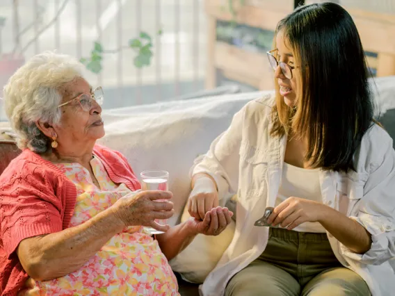 a young woman with brown hair and glasses sits with an older woman holding a glass of water