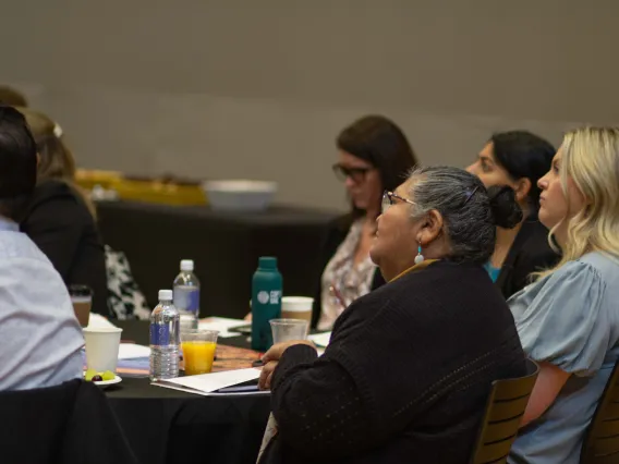 a group of people sit at a table and listen to a speaker