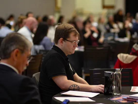 two men sit at a table and listen at a conference