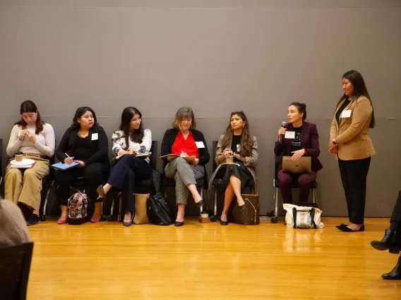 a woman asks a question sitting next to a line of people in chairs