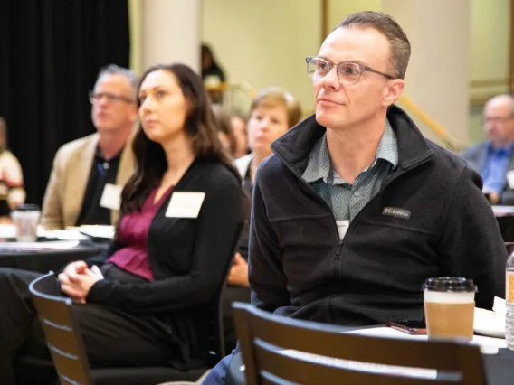 a group of people sit listening to a speaker