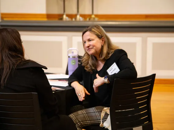 a woman listens to another woman while seated at a round table