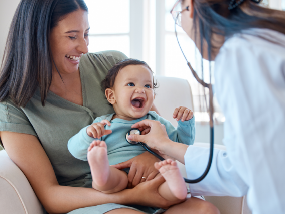 Baby laughing in mothers lap while doctor listens with stethoscope