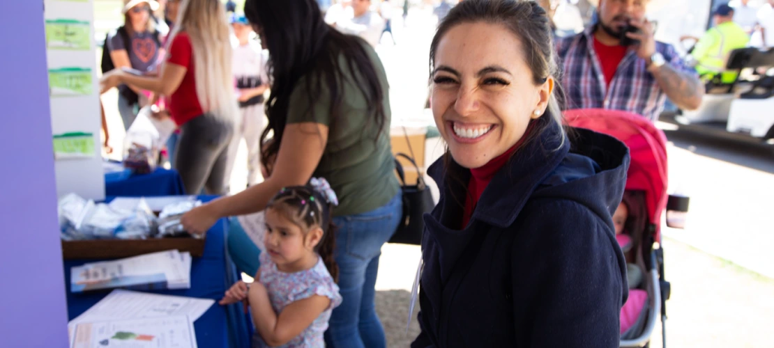 smiling young woman looks at the camera with a young girl and mother in the back ground