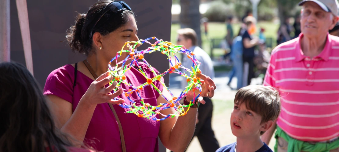 woman demonstrates and expandable toy to a young boy with an older man wearing a baseball cap in the back ground