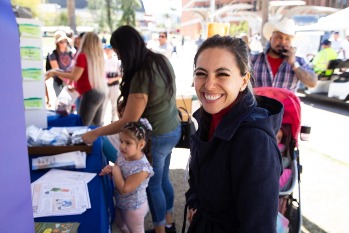 smiling young woman looks at the camera with a young girl and mother in the back ground