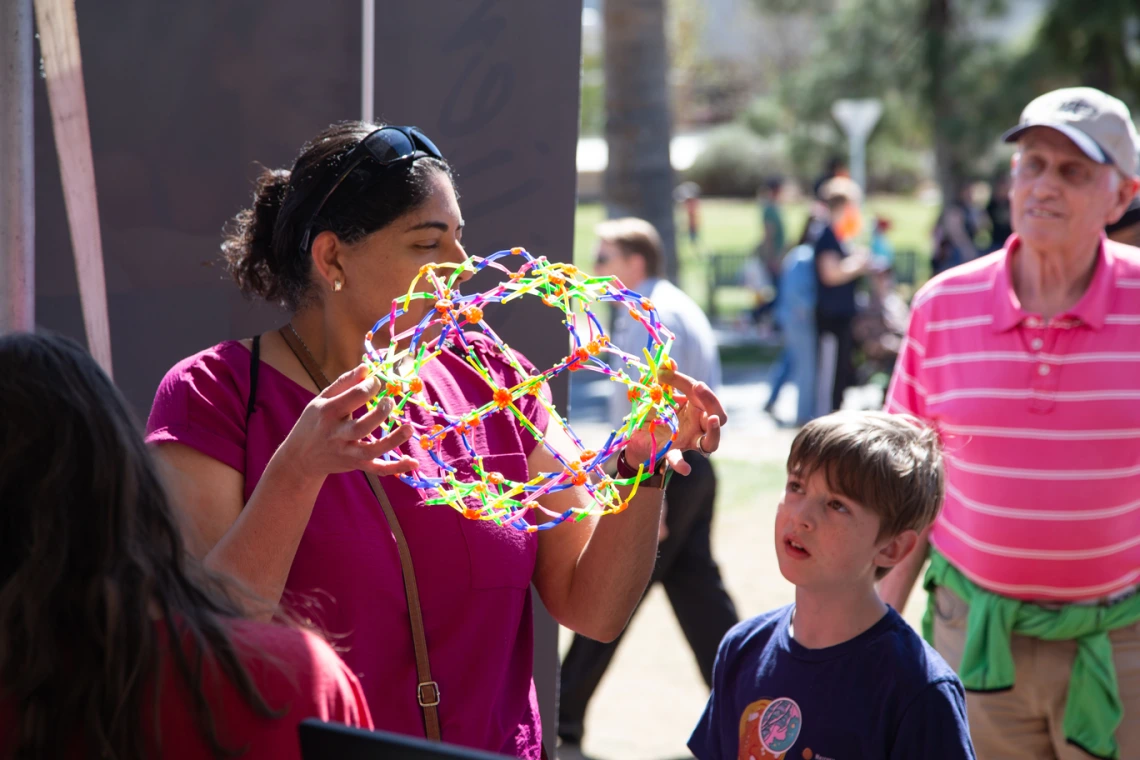 woman demonstrates and expandable toy to a young boy with an older man wearing a baseball cap in the back ground