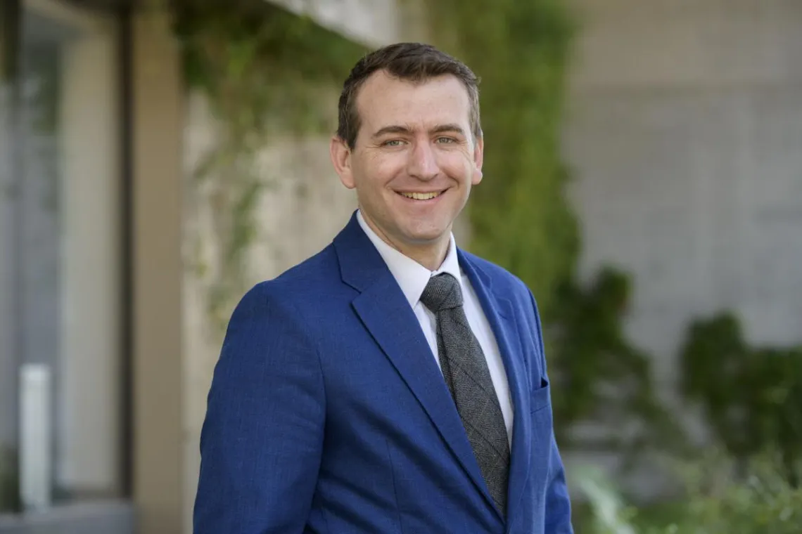 portrait of Benjamin Brady wearing a blue suit in front of some greenery