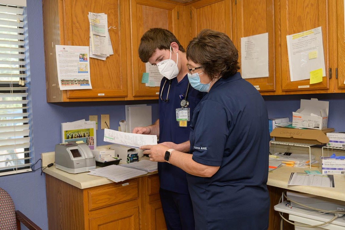 a man and a woman both in blue scrubs and wearing face masks look at papers