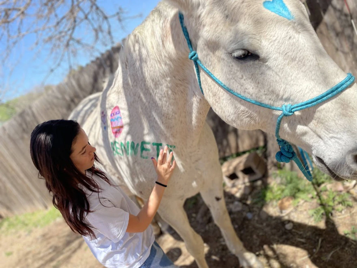 girl finger paints on the shoulder of a white horse