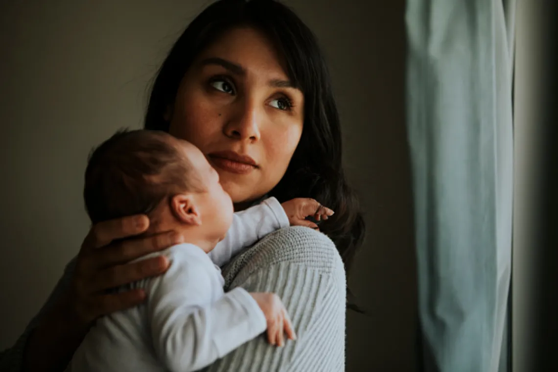 woman holding an infant looking over her shoulder out a window