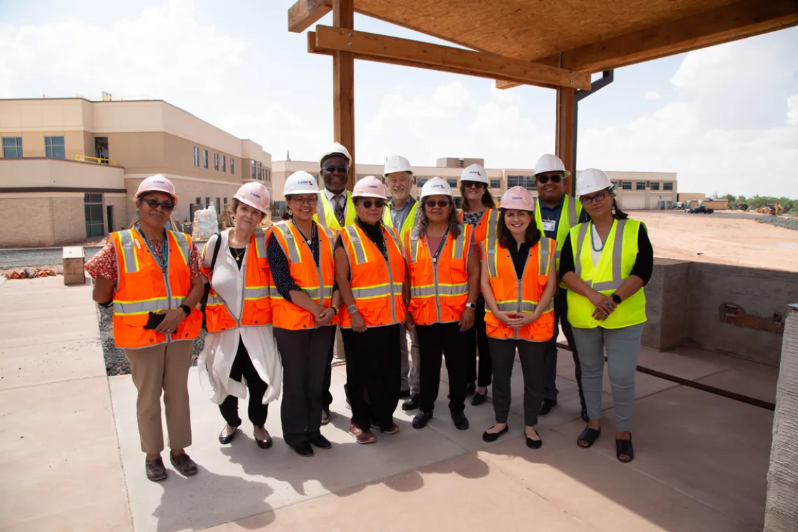 a group of people wearing hard hats and safety vests in front of a building site