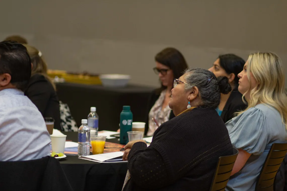 a group of people sit at a table and listen to a speaker