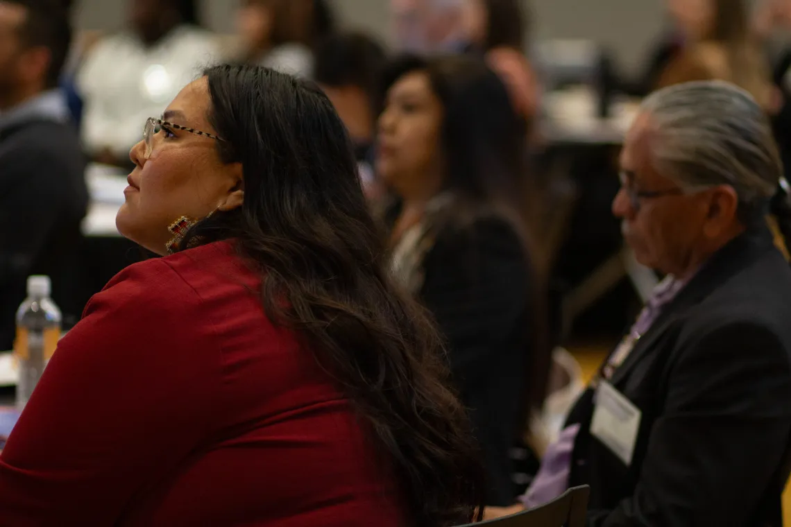 a woman wearing a red top listens to a speaker