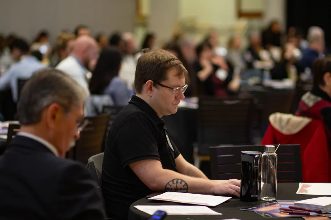 two men sit at a table and listen at a conference