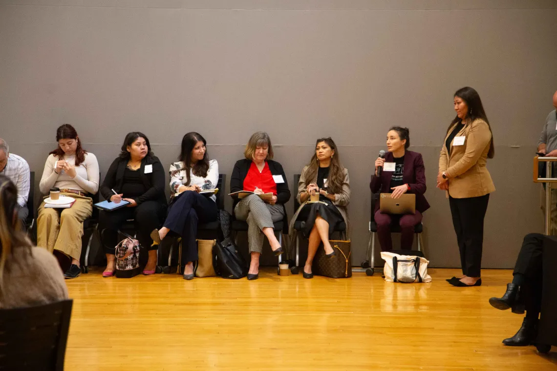 a woman asks a question sitting next to a line of people in chairs