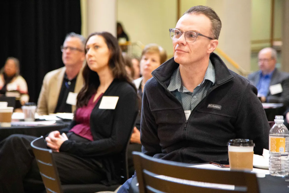 a group of people sit listening to a speaker