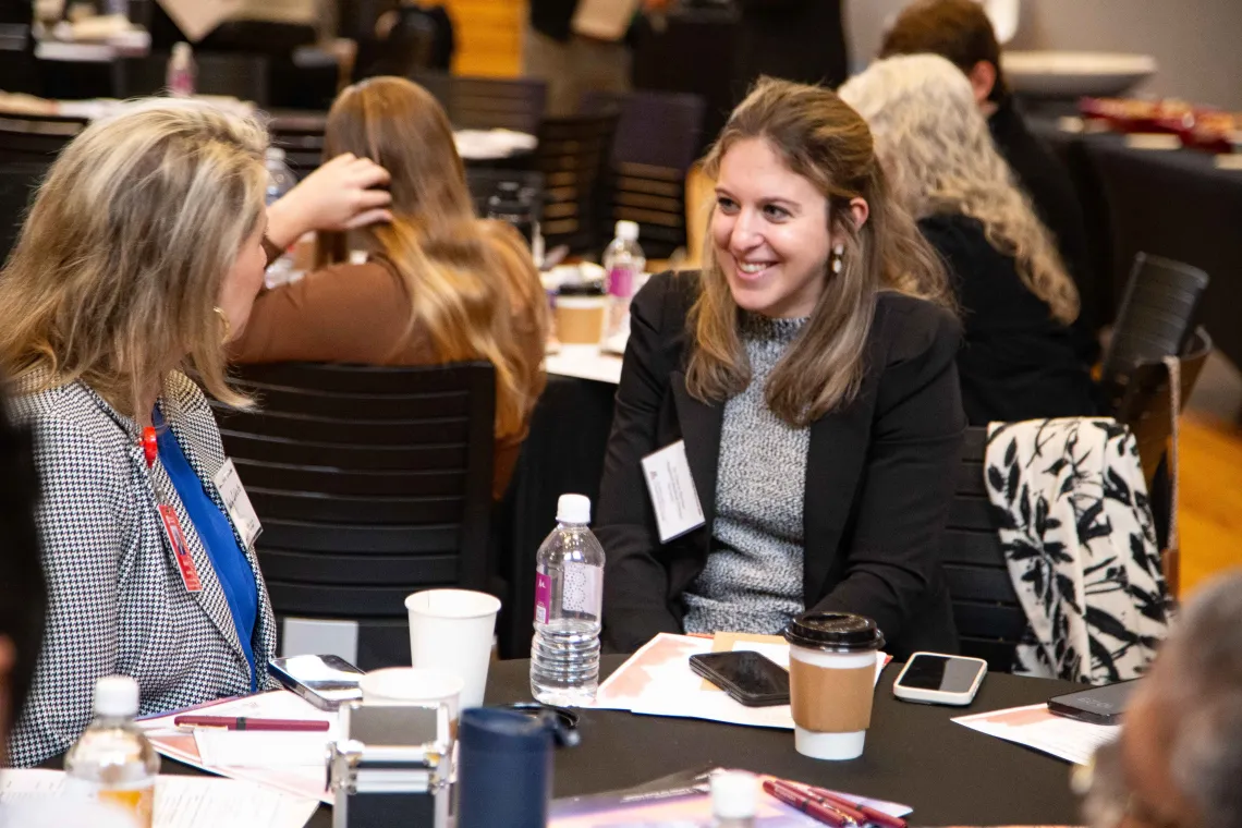 two women share a laugh while sitting at a table covered in a black table cloth