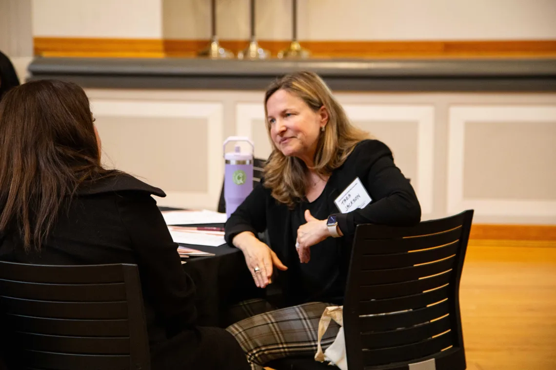 a woman listens to another woman while seated at a round table