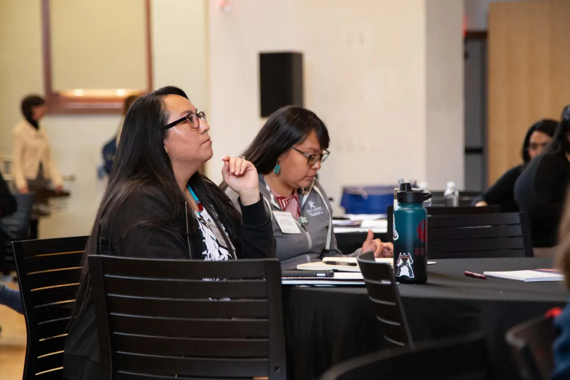 two women sit at a round table listening to a speaker