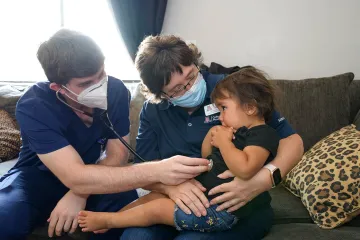 Dr. Hunt holds Amara Lopez while Winkleman listens to her heart during a home health visit