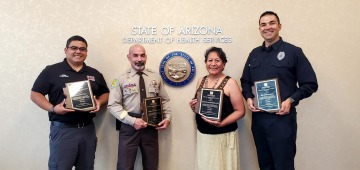 four people holding award plaques in front of the State of Arizona sign