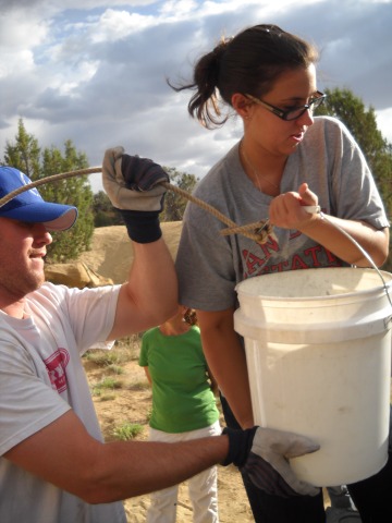 a man and a woman helping to lift a white bucket