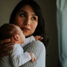 woman holding an infant looking over her shoulder out a window